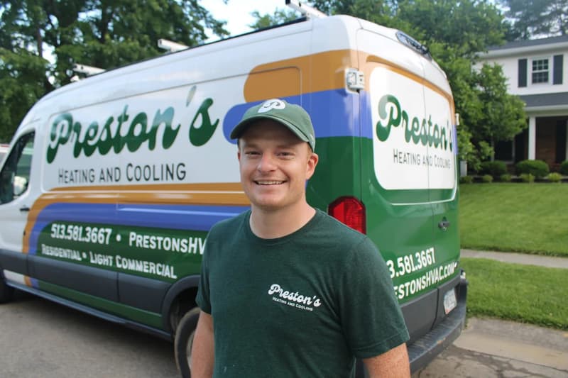 Technician in green cap standing beside Preston's Heating and Cooling van