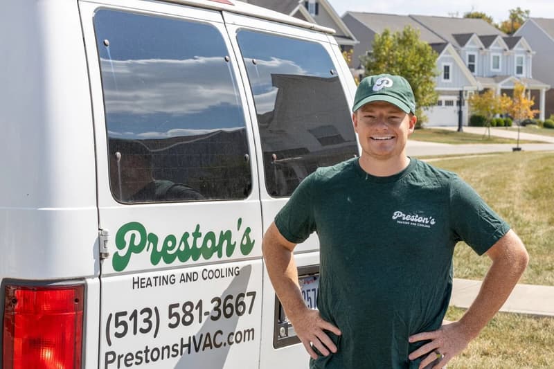 Smiling technician with arms on hips beside company van
