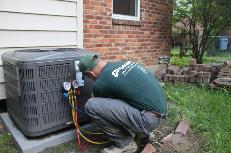 Technician connecting gauges to outdoor air conditioning unit